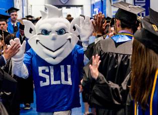 The SLU Billiken offers high fives to students wearing graduation caps and gowns.