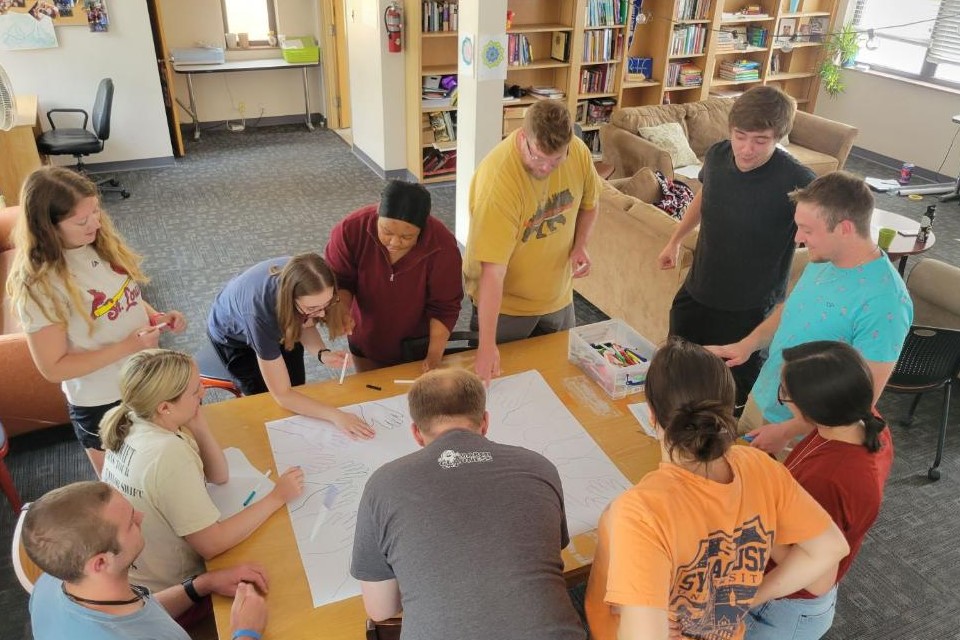 Program participants stand around a table and examine a large piece of paper placed in the middle.